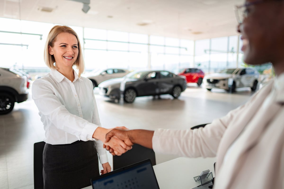 Two women shaking hands and smiling after making a successful deal at car dealership