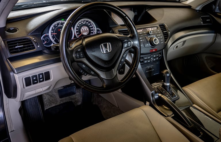 Honda car interior showing black steering wheel, beige leather seats, dashboard with gauges, and center console controls