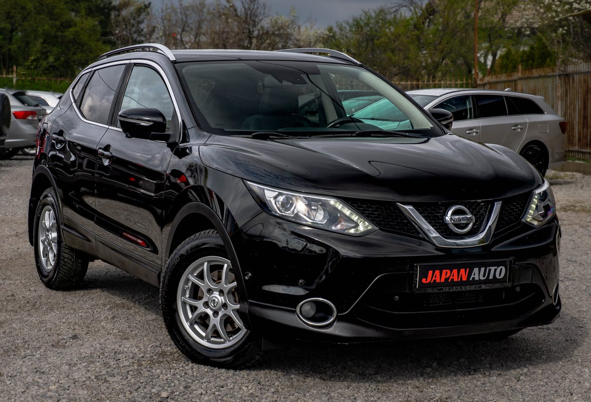 Black Nissan Qashqai SUV parked in a lot with trees in background and Japan Auto dealership plate visible