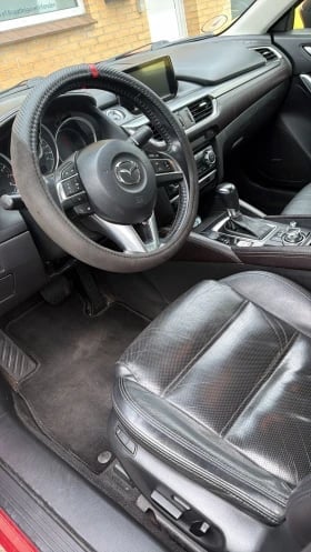 Car interior showing steering wheel, dashboard with touchscreen display, and leather seats with carbon fiber accents