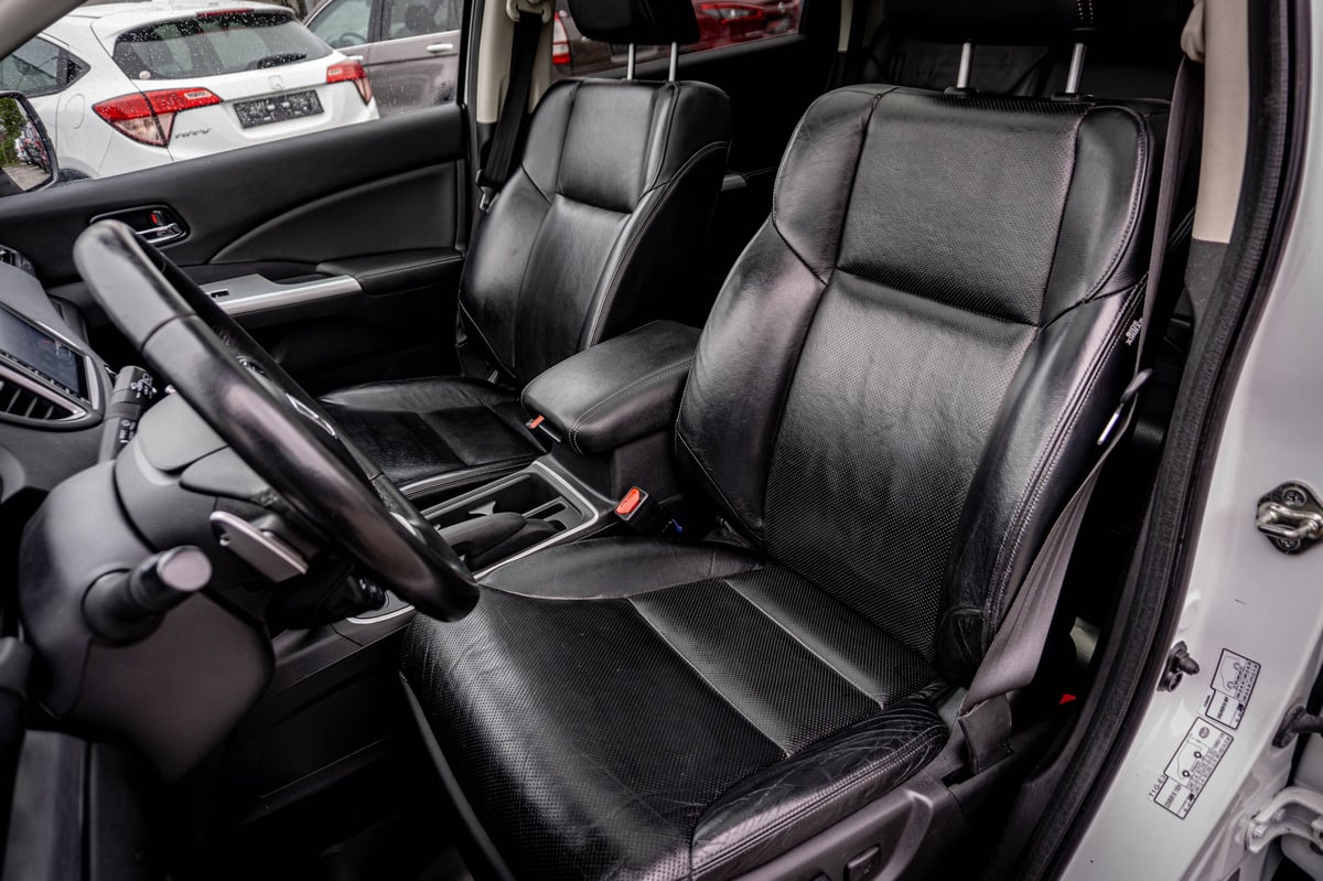 Black leather car interior with steering wheel and front seats visible through open drivers side door