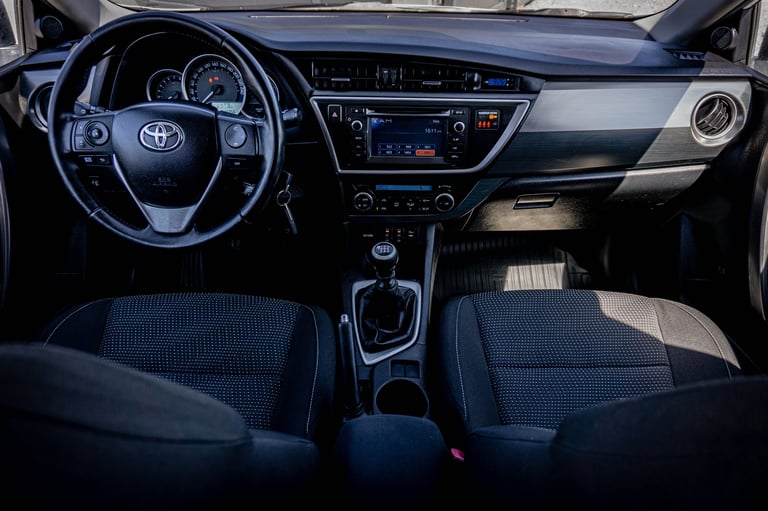 Interior of Toyota vehicle showing steering wheel, dashboard, touchscreen display, and front seats with blue and black upholstery