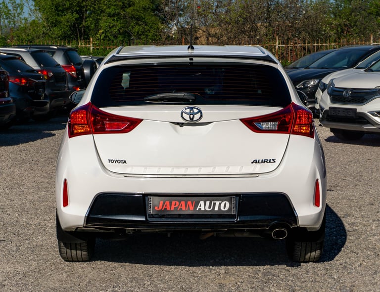 White Toyota Auris hatchback car parked in a lot, rear view showing taillights and Japan Auto license plate