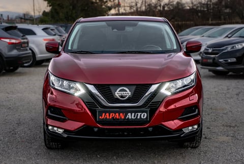 Red Nissan SUV with Japan Auto license plate displayed at a car dealership lot with other vehicles in background