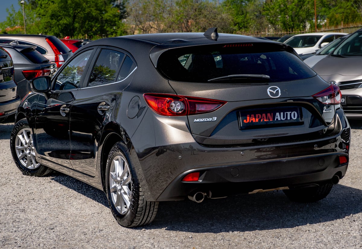 Black Mazda sedan displayed at outdoor car dealership lot with other vehicles visible in background