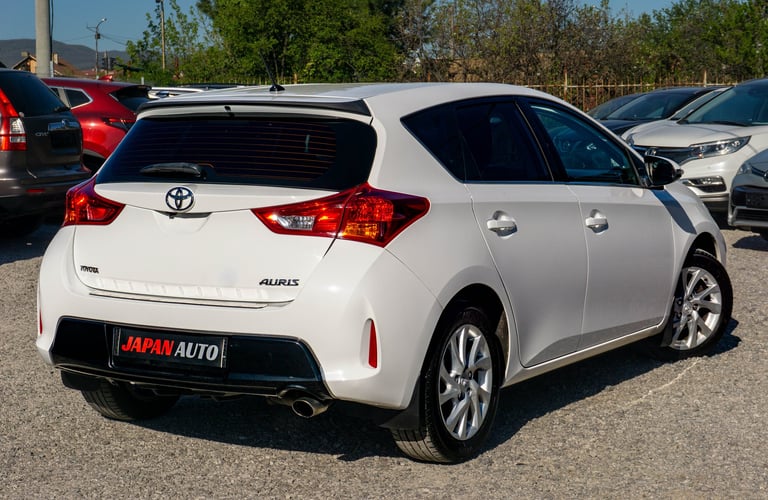 White Toyota Auris hatchback parked at a dealership lot, rear three-quarter view with other vehicles visible in background