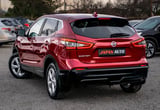 Red Nissan Qashqai compact SUV parked in a lot, rear three-quarter view with Japan Auto dealership badge