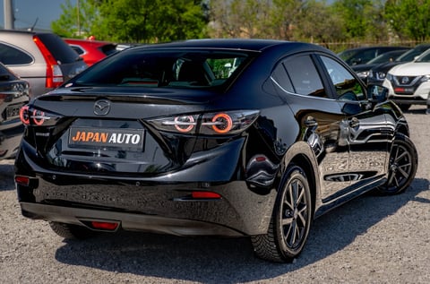 Black Mazda sedan with orange accents parked at a dealership lot with Japan Auto sign visible