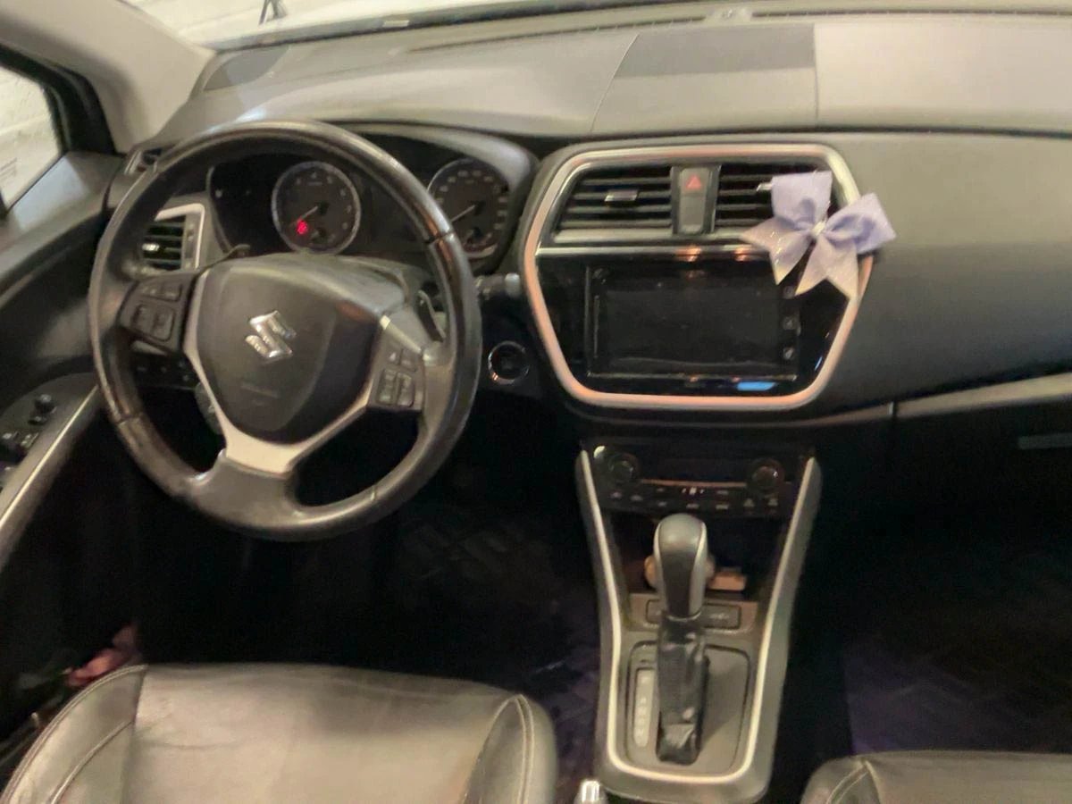 Car interior showing steering wheel, dashboard with touchscreen display, and purple gift bow on rearview mirror