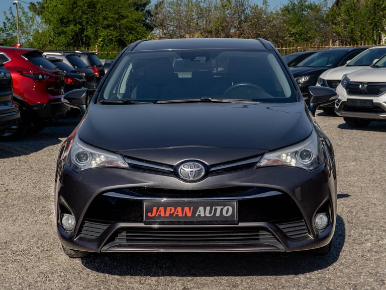 Front view of a dark gray Toyota car at a dealership with JAPAN AUTO sign, parked among other vehicles