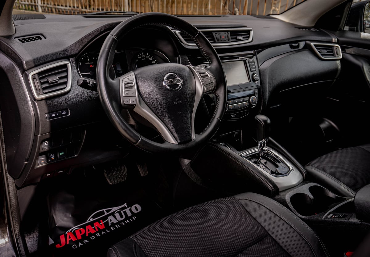 Interior view of a Nissan vehicle showing steering wheel, dashboard, and black leather seats with wood railing visible through windshield