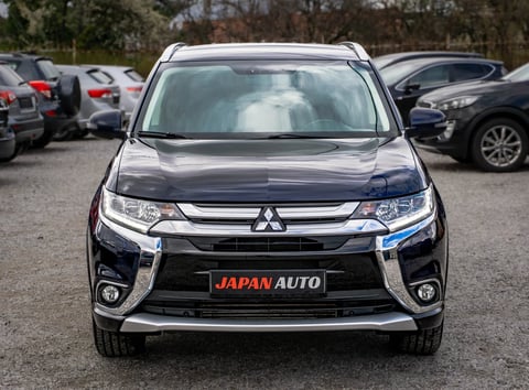 Front view of a black Mitsubishi SUV with JAPAN AUTO license plate in a dealership lot surrounded by other vehicles