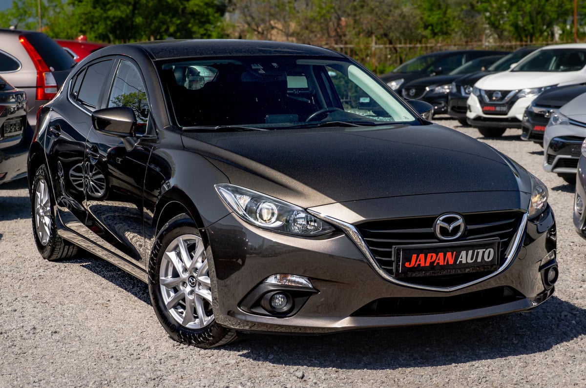 Black Mazda compact sedan displayed at a car dealership lot with other vehicles in the background