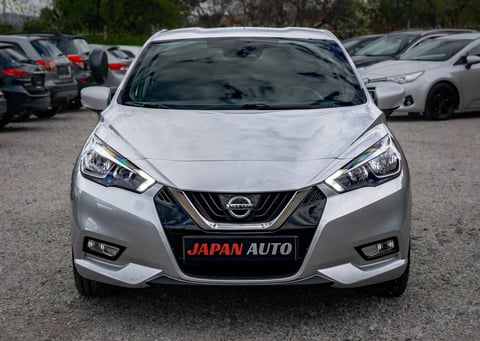 White Nissan sedan with Japan Auto license plate displayed in a car dealership lot with other vehicles in background