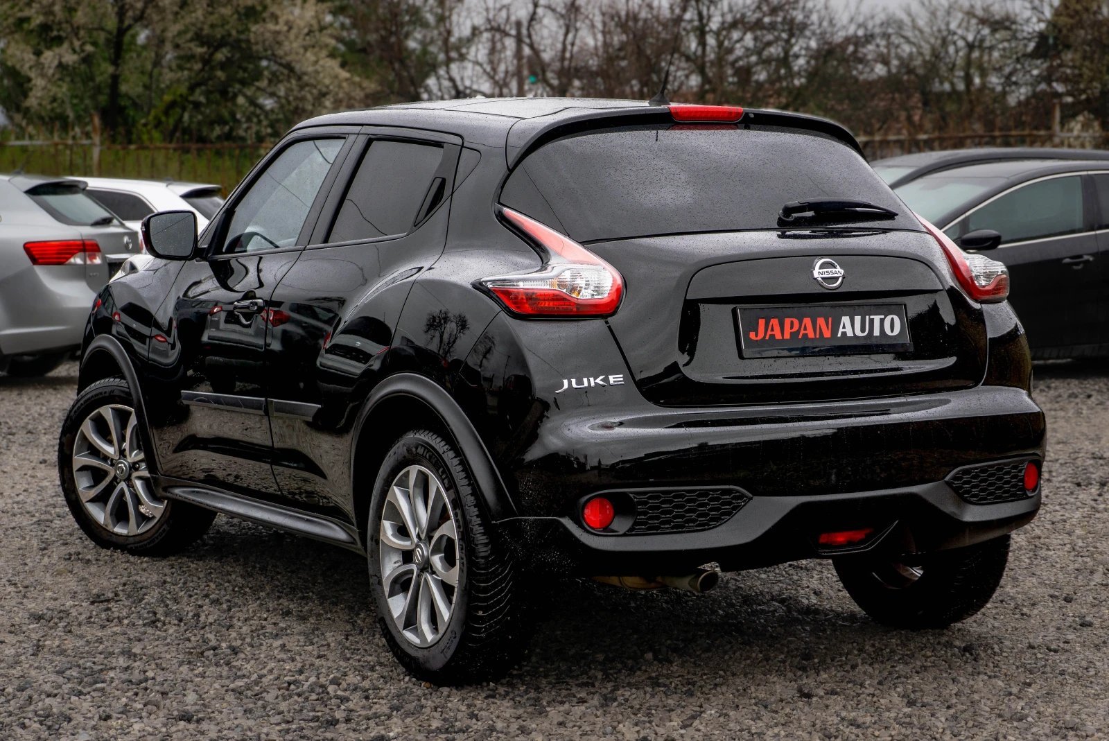 Black Nissan Juke compact SUV parked at a dealership lot with other vehicles in the background
