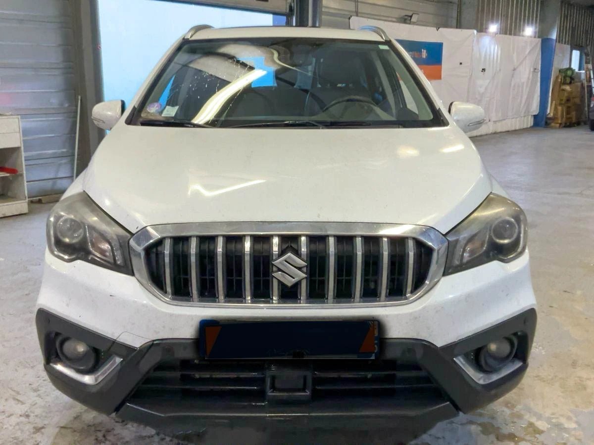 Front view of a white Maruti Suzuki SUV with distinctive vertical grille in an indoor garage or warehouse setting