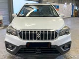 Front view of a white Maruti Suzuki SUV with distinctive vertical grille in an indoor garage or warehouse setting