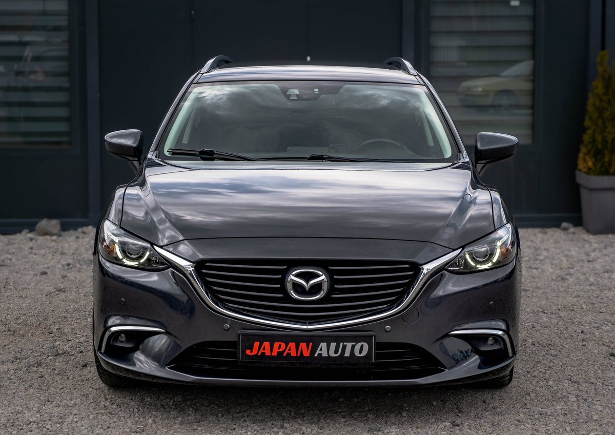 Front view of a black Mazda V6 sedan with Japan Auto dealership plate parked in front of a dark building