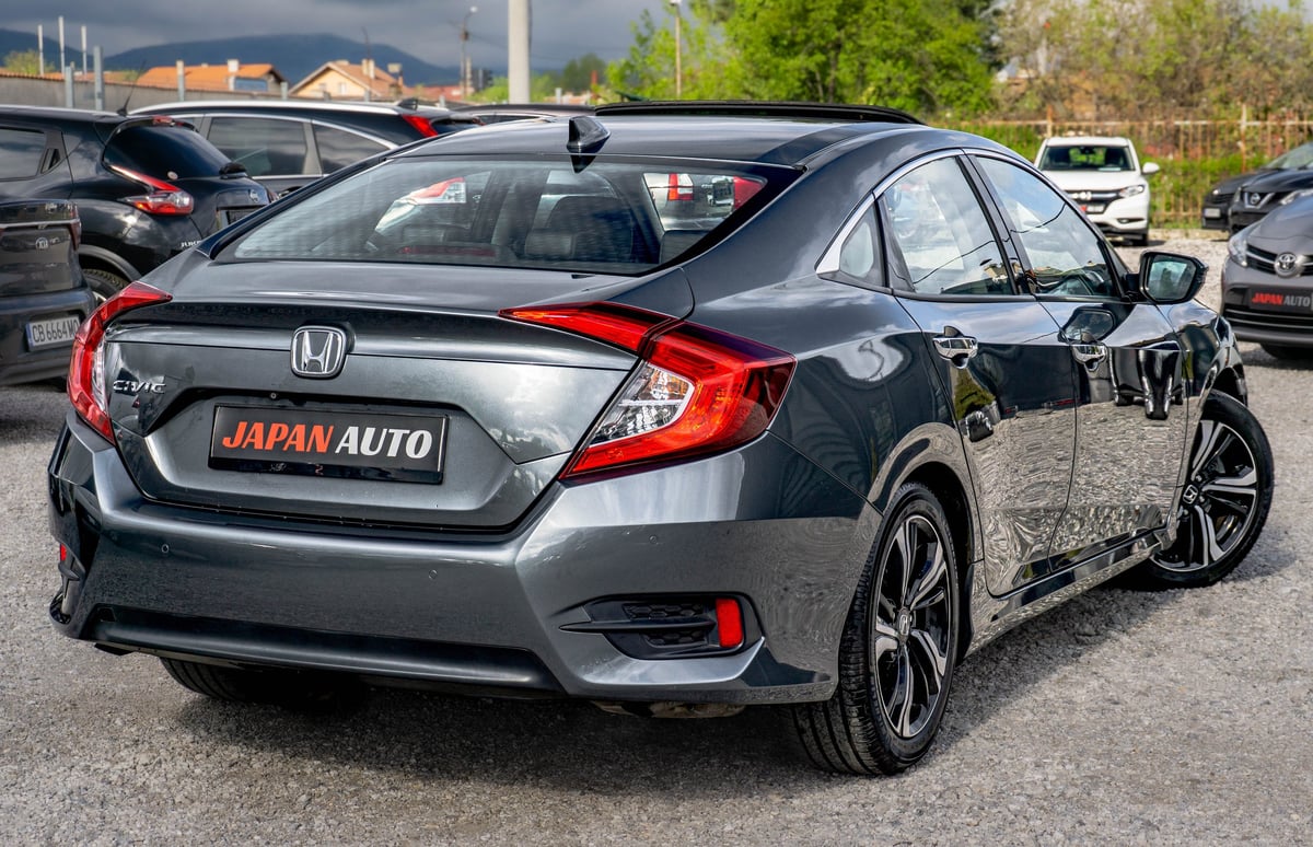 Silver Honda sedan with red taillights parked at a dealership lot with other vehicles visible in background