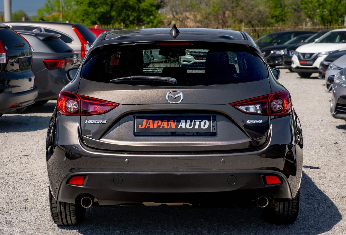 Black Mazda hatchback car parked at a dealership lot with Japan Auto signage visible on the rear bumper
