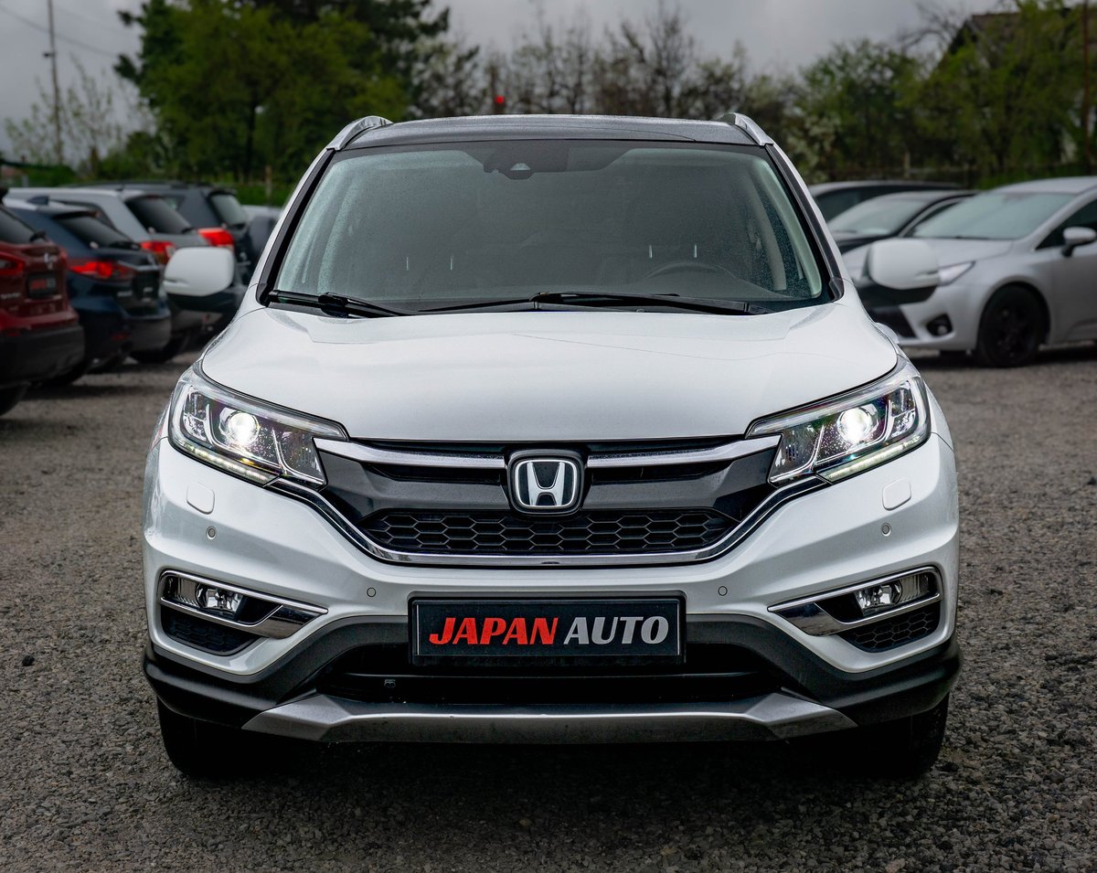 White Honda CR-V SUV parked in a dealership lot with Japan Auto signage and other vehicles visible in background