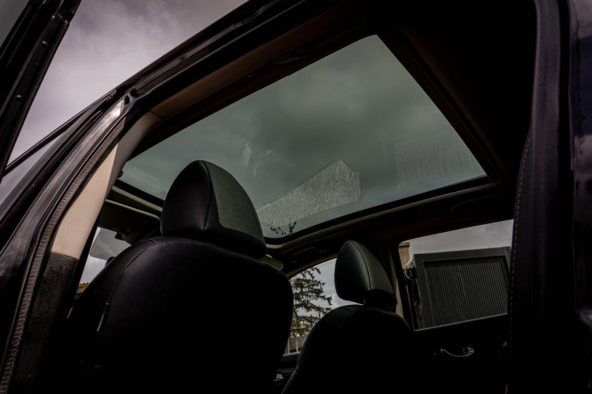 Interior view of a car with black seats and an open panoramic sunroof, showing a cloudy sky above