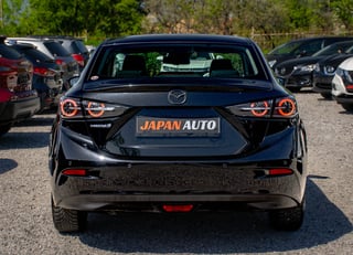 Black Mazda sedan viewed from rear, with Japan Auto dealership sign, parked among other vehicles
