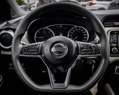 Nissan steering wheel with leather grip, centered logo, and dashboard gauges visible behind it in a parked vehicle