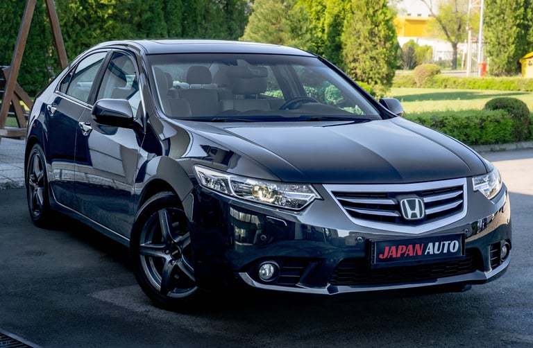 Black Honda sedan parked in driveway with Japan Auto license plate, surrounded by green landscaping