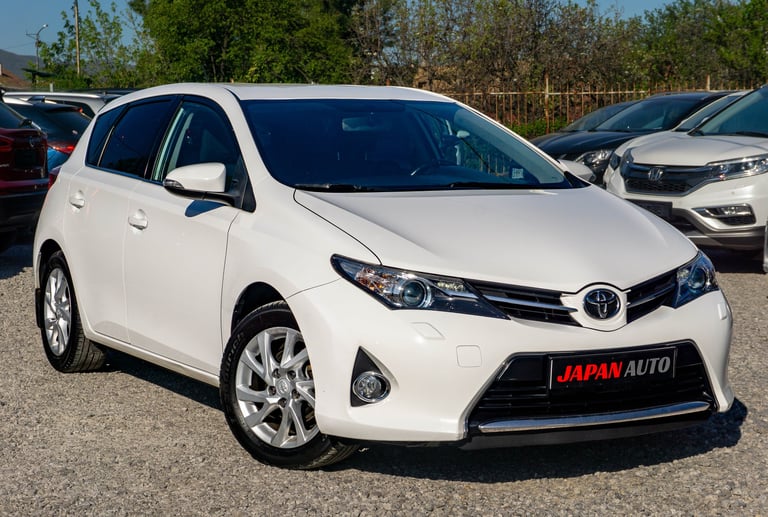 White Toyota Auris hatchback on display at a car dealership lot with other vehicles visible in the background
