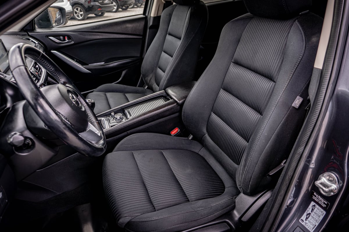Black car interior with ribbed front seats, steering wheel, and dashboard visible from driver side