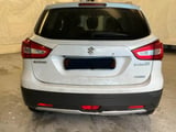 Rear view of a white Suzuki SX4 compact SUV parked indoors, showing red taillights and license plate area