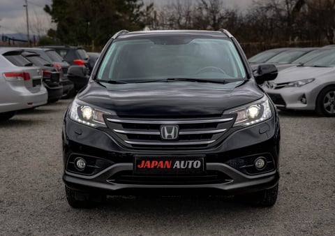 Black Honda CR-V SUV photographed head-on at a car dealership lot with other vehicles visible in background