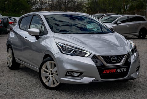 Silver Nissan Micra hatchback on a car lot, viewed from the front angle, with other vehicles visible in background