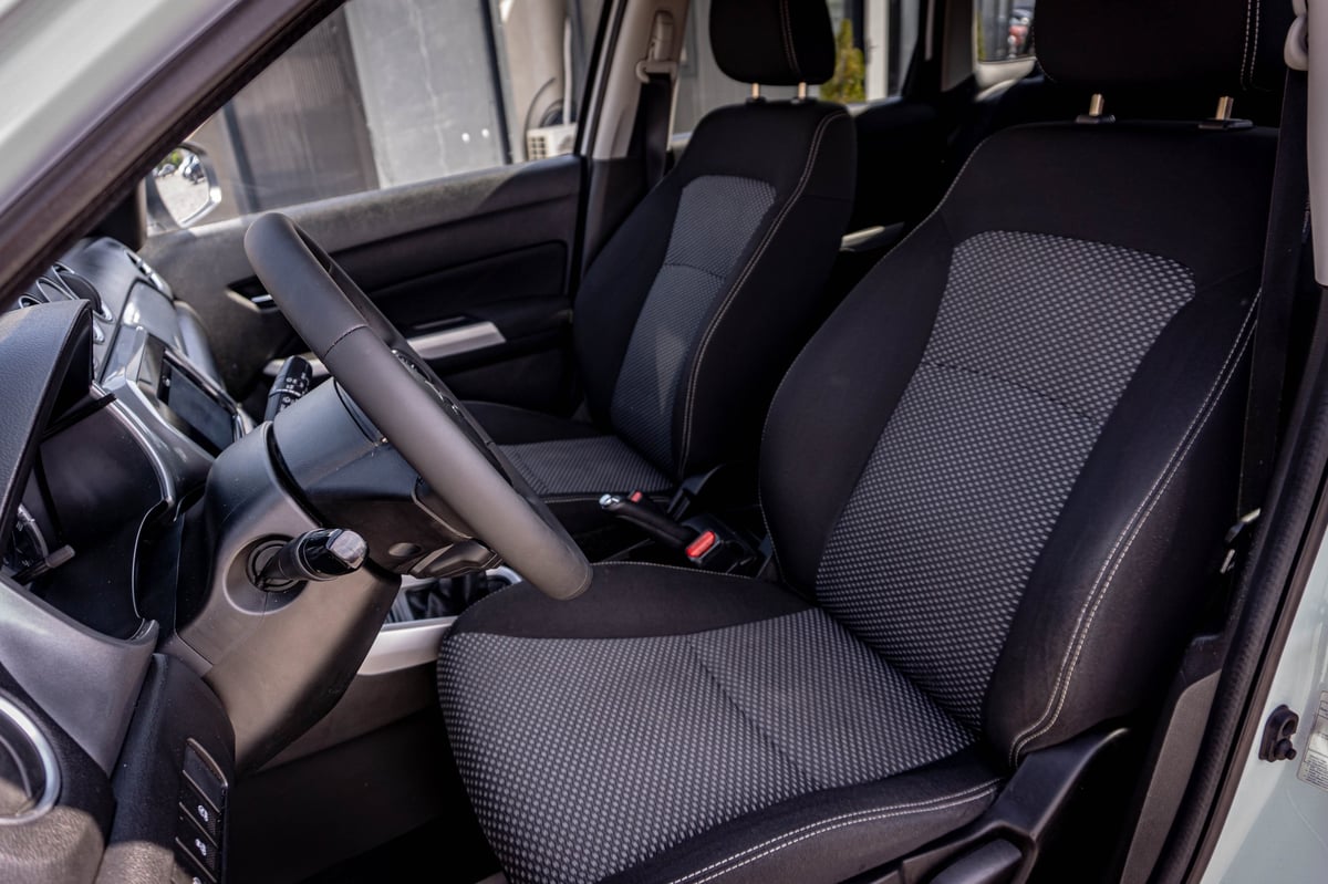 Interior view of a compact car showing black and gray seat covers, steering wheel, and dashboard with left-side driving position