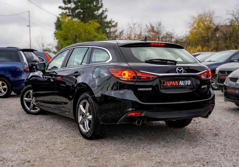 Black Mazda sedan viewed from rear angle in an outdoor parking lot with other vehicles visible