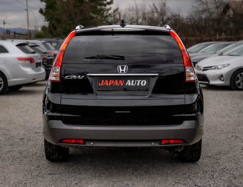 Rear view of a black Honda CR-V with red taillights and Japan Auto license plate, parked in a lot with other vehicles