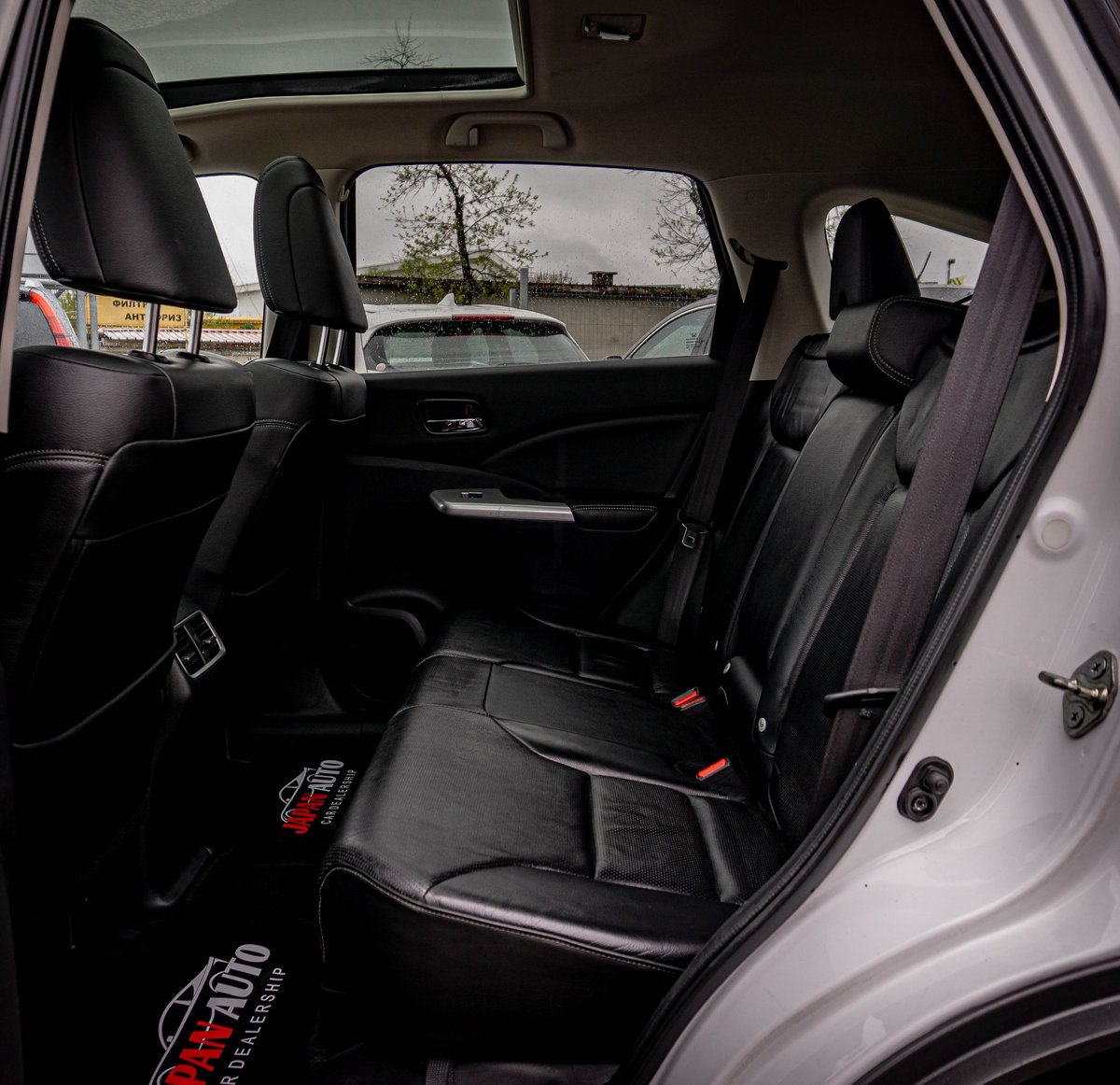 Interior view of a vehicle showing the back seat with black leather upholstery and safety features visible through the rear window