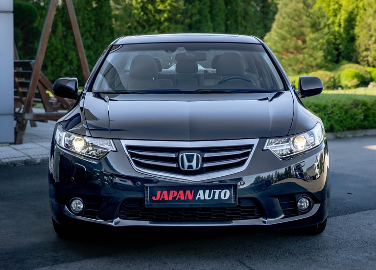 Front view of a black Honda sedan with Japan Auto license plate in a driveway surrounded by green hedges