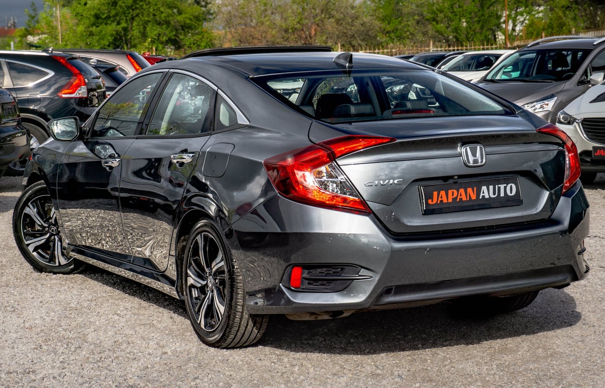 Gray Honda Civic sedan at a dealership lot with Japan Auto signage, surrounded by other vehicles
