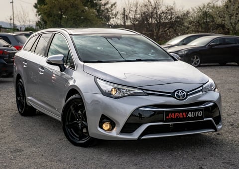 White Toyota Avensis SUV parked in a lot with bare trees in background