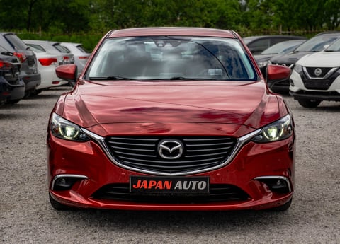 Red Mazda sedan with Japan Auto license plate parked in a dealership lot with other vehicles visible in background