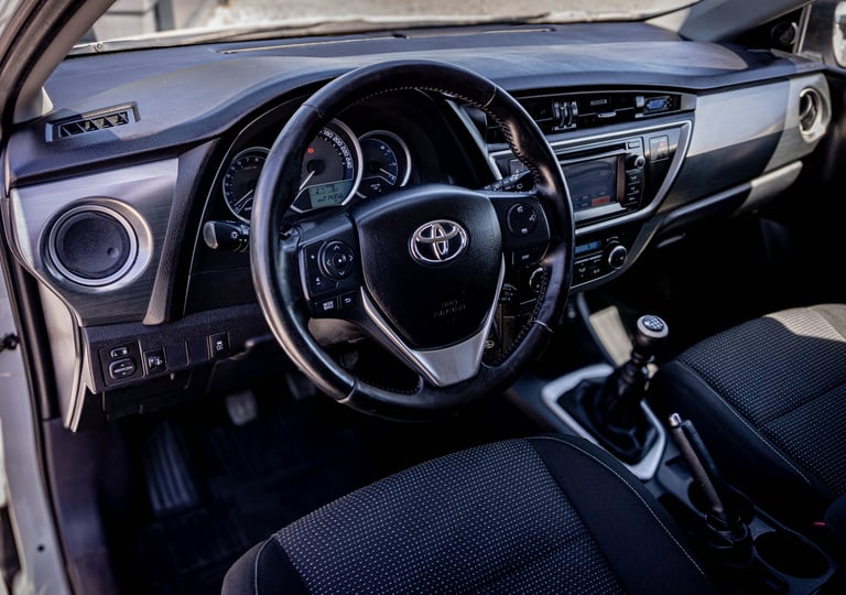 Interior view of a Toyota vehicle showing black steering wheel, dashboard with blue accents, and black upholstered seats