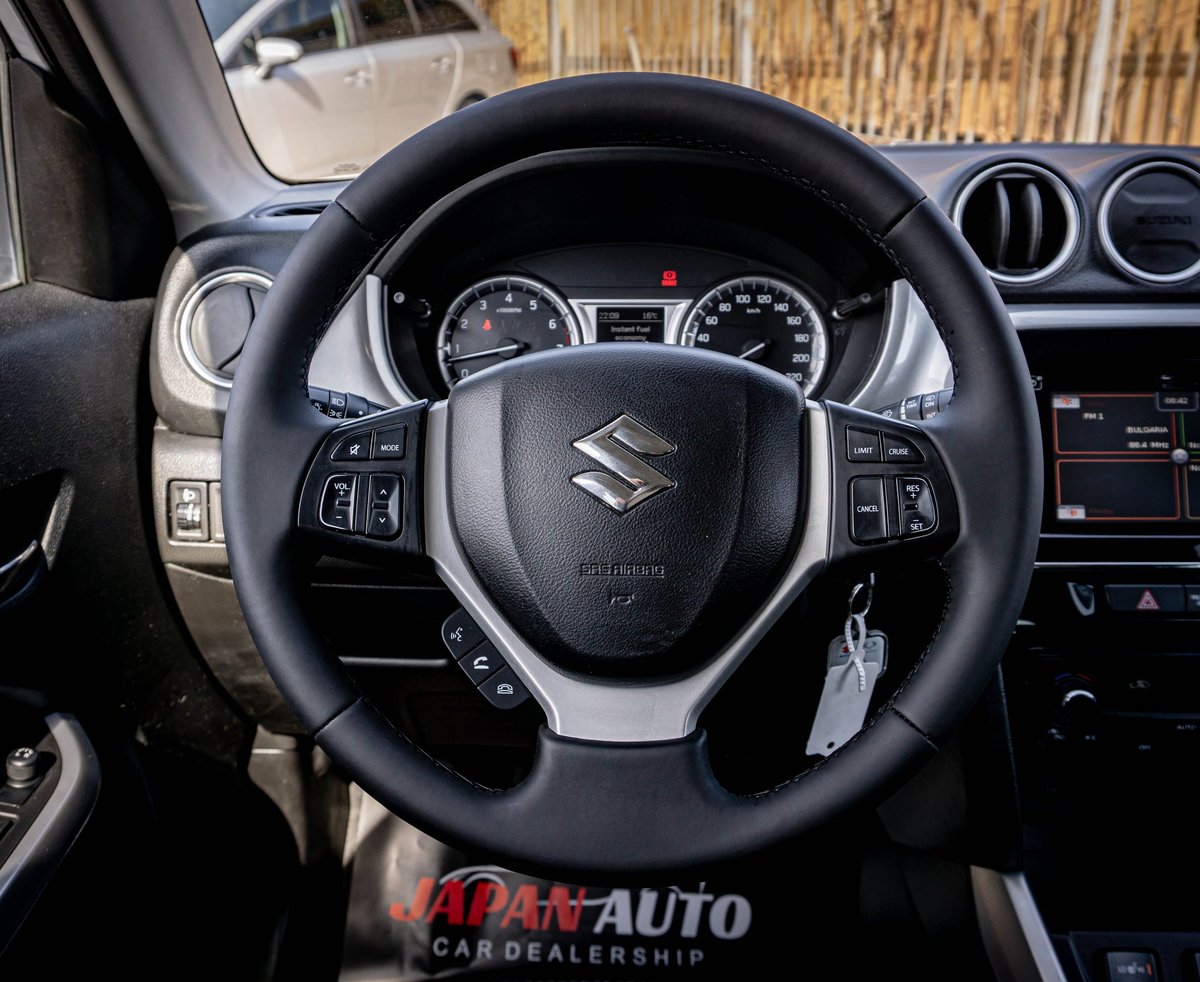Close-up view of a Suzuki car steering wheel and dashboard interior with instrument cluster visible