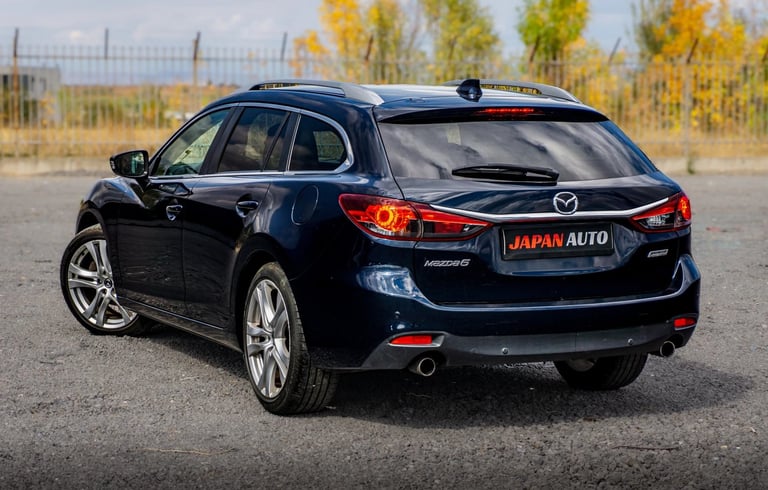 Black Mazda SUV with Japan Auto license plate parked on asphalt lot with autumn trees in background