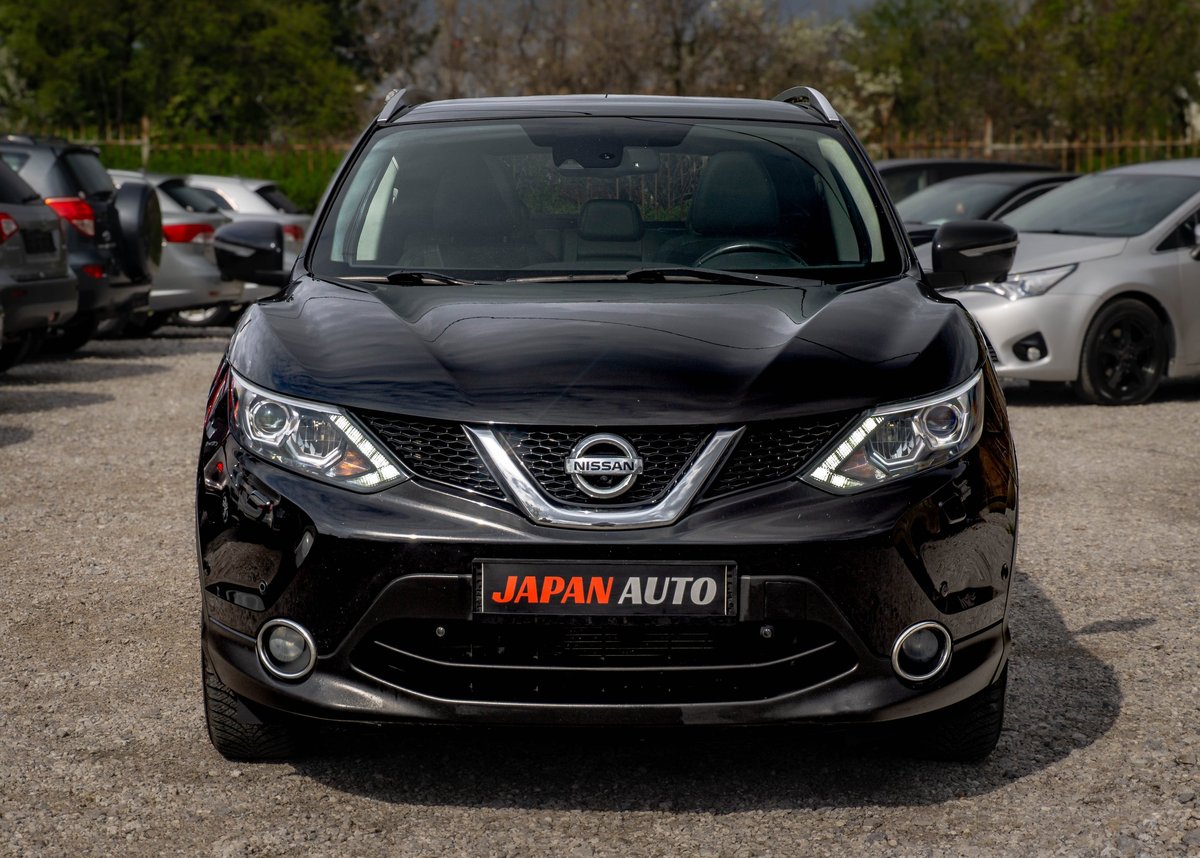 Black Nissan SUV with Japan Auto dealer plate parked in lot with trees and other vehicles in background