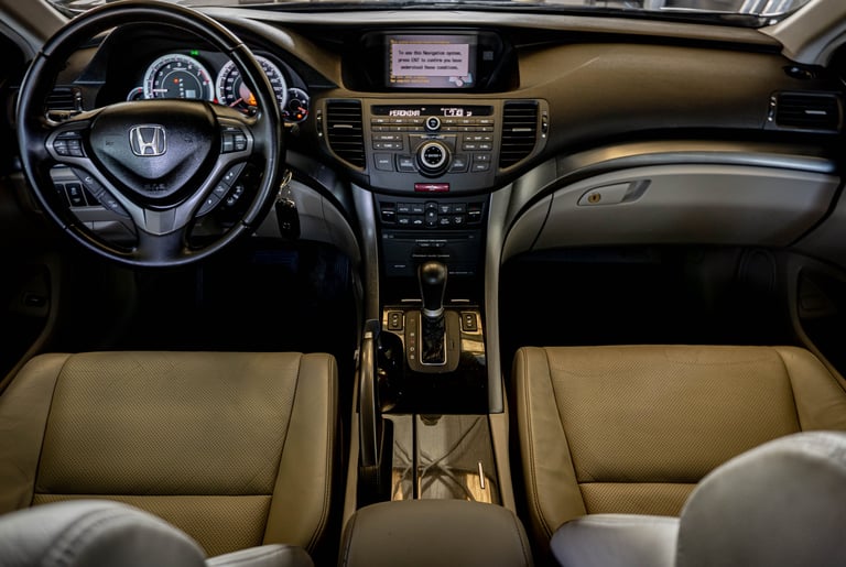 Interior view of Honda vehicle dashboard and steering wheel with tan leather seats and dark trim