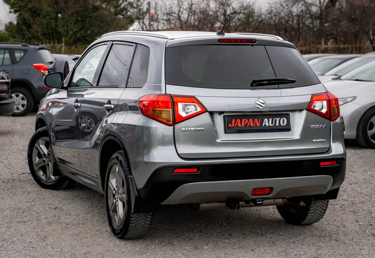 Silver Suzuki compact SUV photographed from rear angle in a parking lot with other vehicles visible