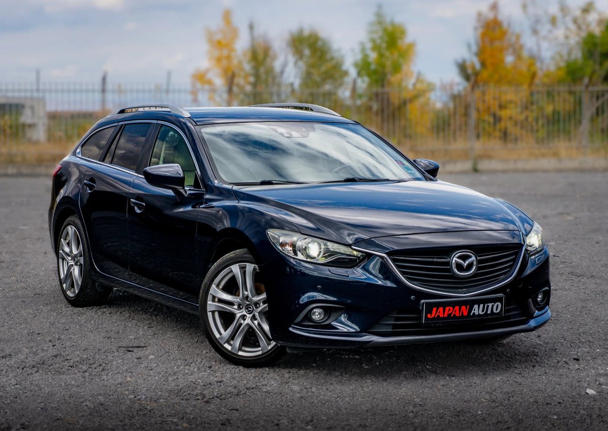 Dark blue Mazda sedan parked on asphalt with autumn trees in background