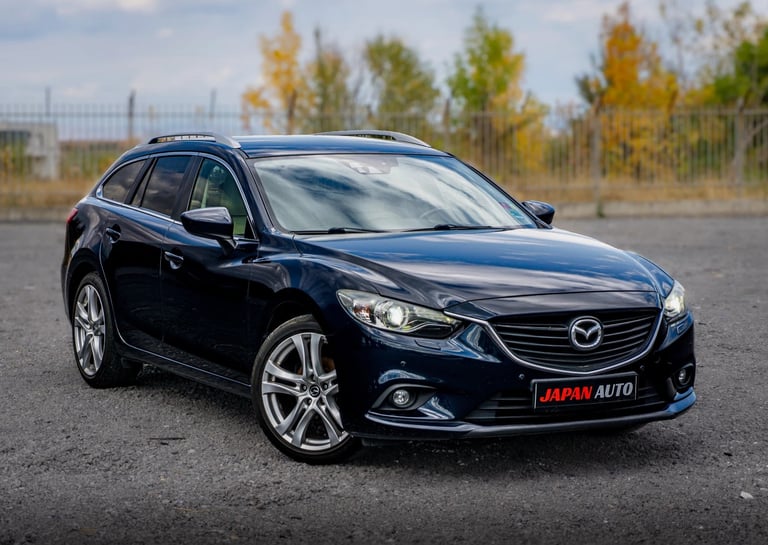 Dark blue Mazda sedan parked on asphalt with autumn trees in background